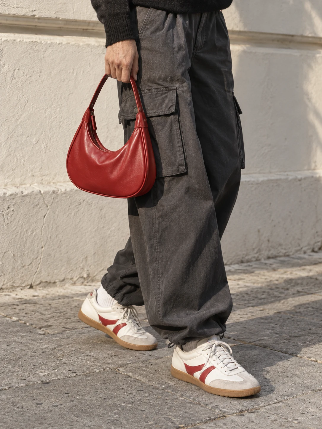 A red leather bag, charcoal cargo trousers, and cream sneakers